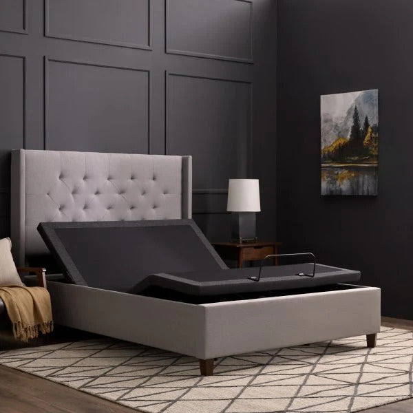 Malouf Gray adjustable bed in a bedroom setting with a tufted headboard and lamp.